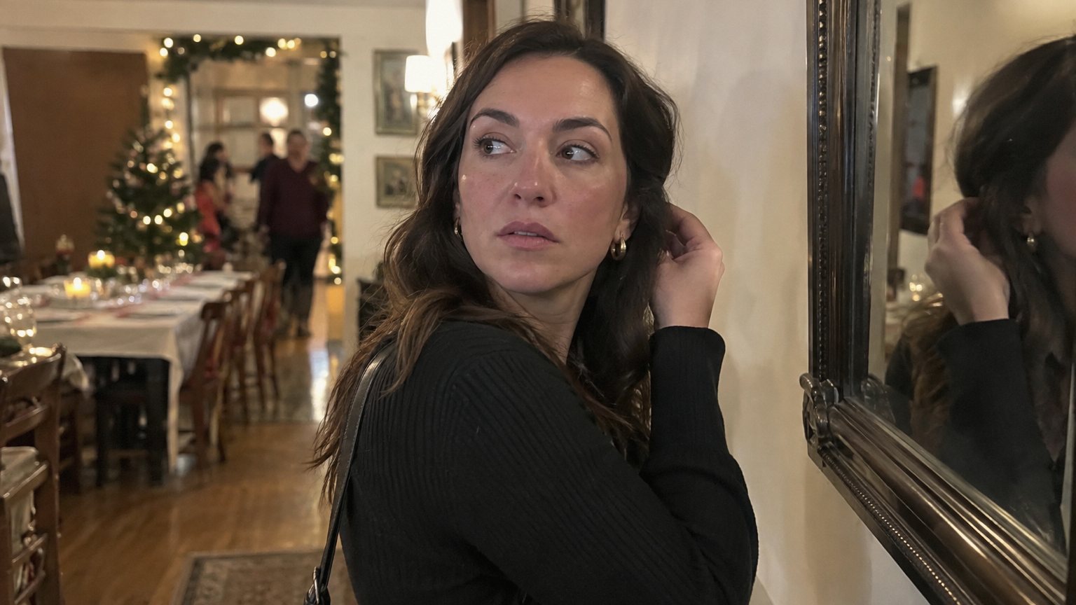 An adult woman checks her face in a phone camera before a group photo at a holiday dinner.